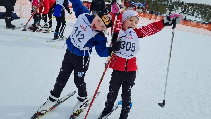 Två glada barn på skidor som sträcker upp armarna i luften.