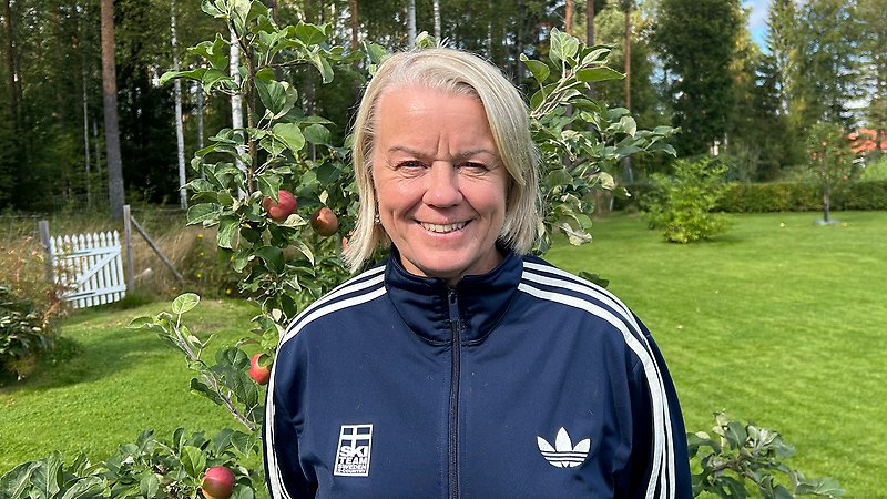 Karin Ersson utomhus framför ett äppelträd, iklädd mörkblå träningsjacka med Ski Team Sweden-logotyp.